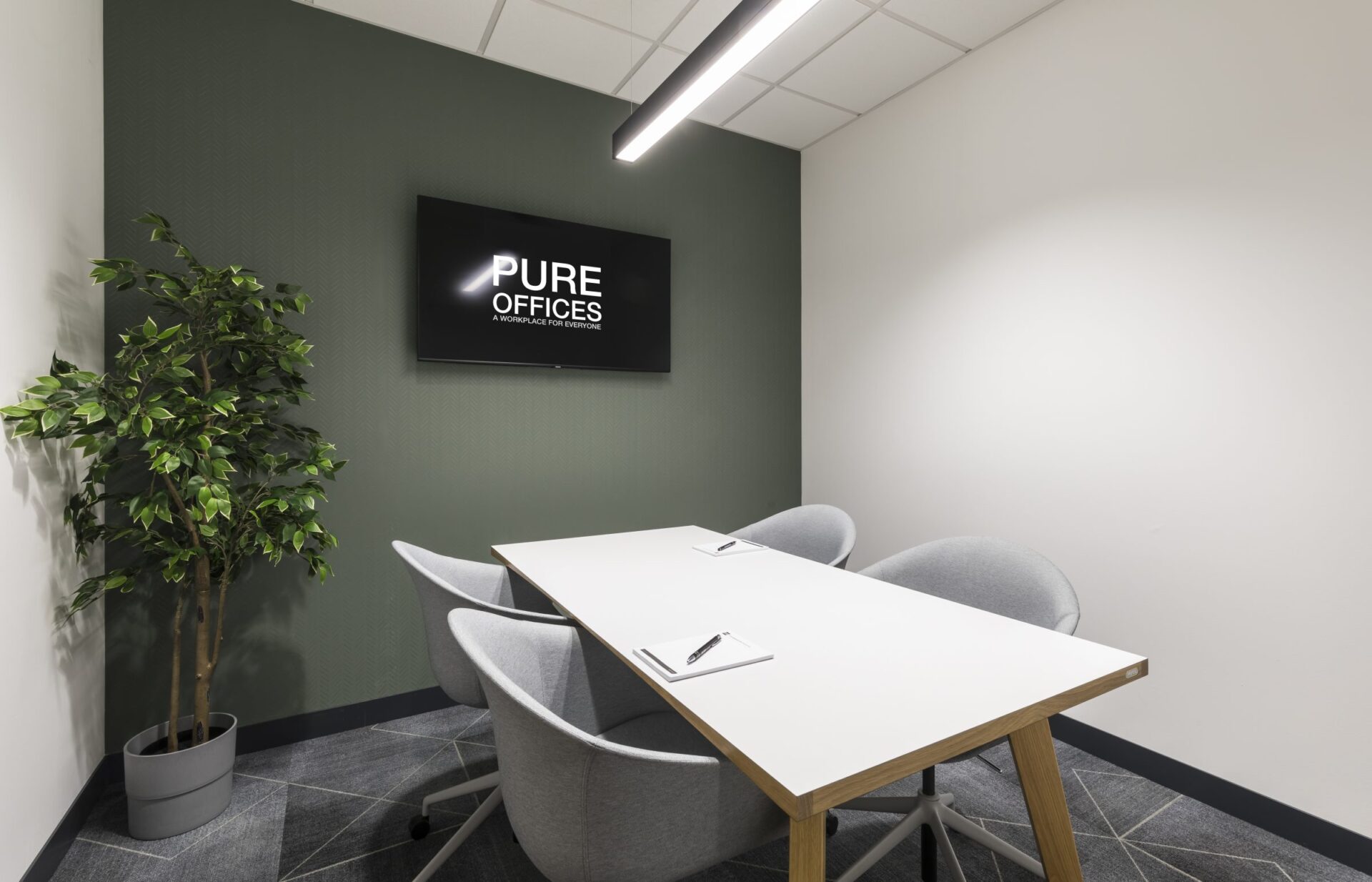 Minimalist meeting room in Edinburgh Park, featuring a rectangular white table, four gray chairs, and a potted plant. A wall-mounted TV displays PURE OFFICES. The space is accented with green and white walls and has a tiled floor.