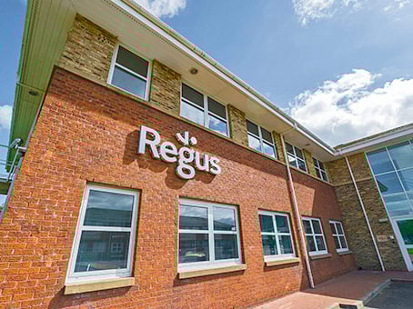 The exterior view of the Regus office building at 8 Deer Park showcases red brick walls and expansive windows. The Regus logo stands out prominently, while the partly cloudy sky casts sunlight, illuminating the facade beautifully.