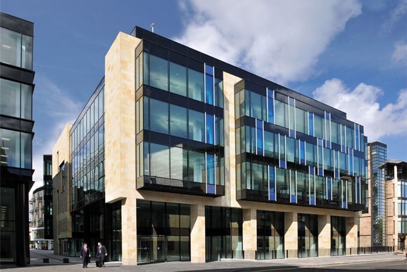 Modern glass and stone office building with reflective windows and blue vertical accents in the heart of Edinburgh City Centre. The structure is set against a partly cloudy sky, with two people walking on the street nearby.