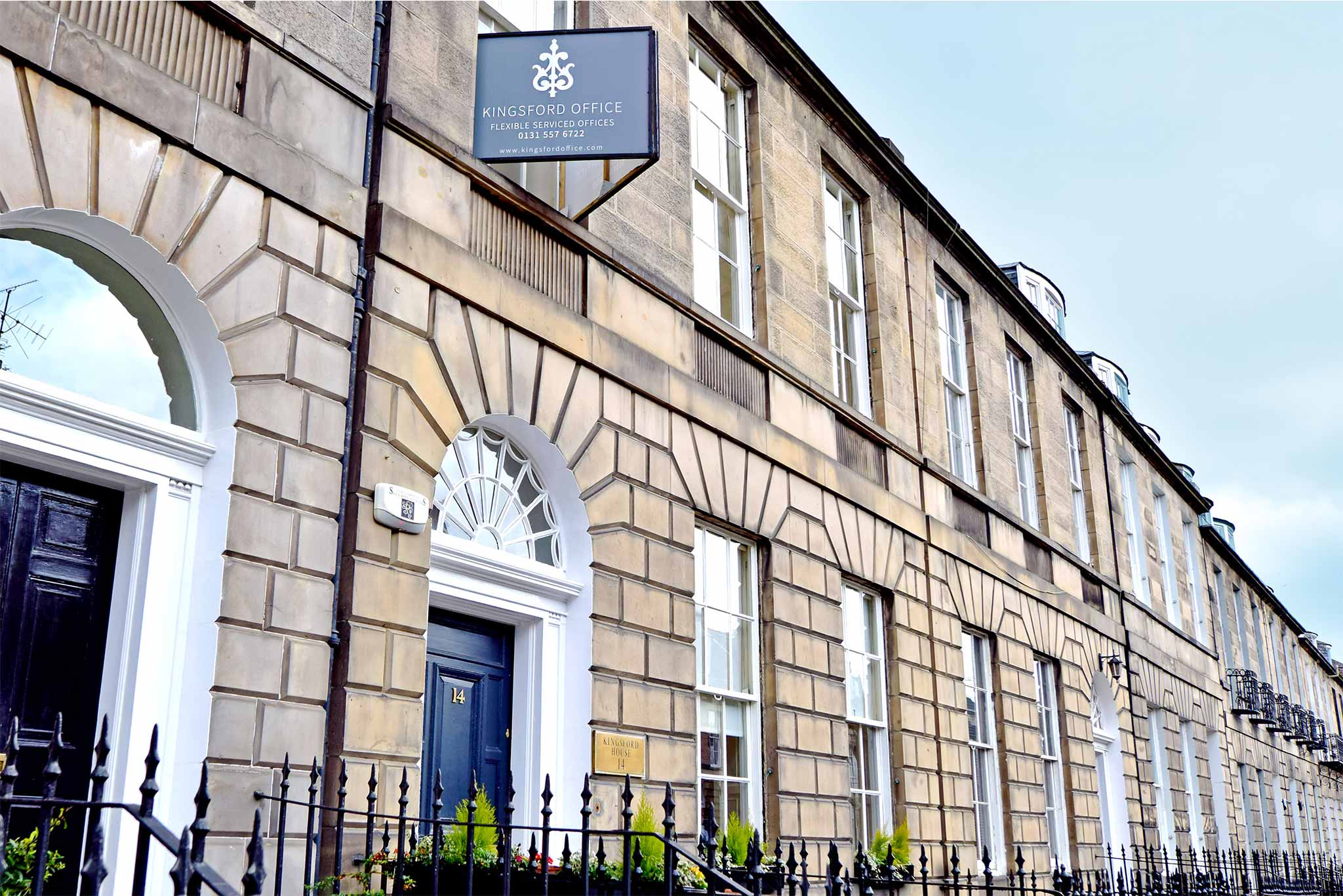 A row of classic, stone-faced buildings with large, arched windows and black doors on 14 Albany Street. Above one door, theres a sign that reads Kingsford Office. A black metal fence lines the front, with small bushes visible near the doors.