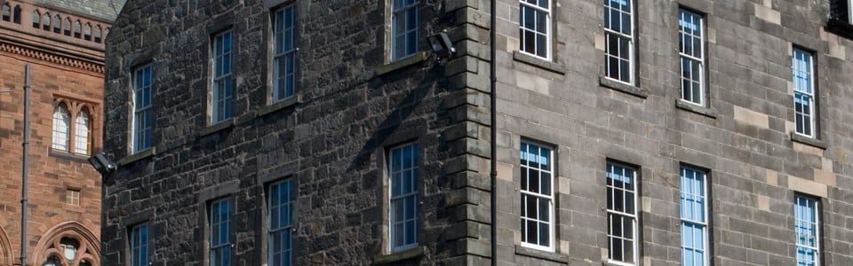A corner view of two connected stone buildings with multiple windows graces North St David Street. The left building features darker stone, while its neighbor displays a lighter hue. In the background, a red brick structure peeks into view, adding contrast to the historic charm.