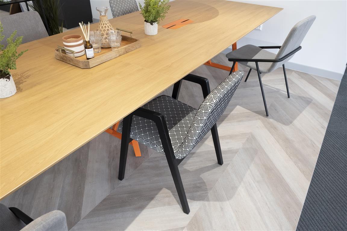 Verdant plants bring a touch of nature to this modern meeting room, featuring a long wooden table surrounded by patterned and plain chairs on a beige carpet. A tray with cups, a carafe, and an incense holder complement the greenery, creating a refreshing atmosphere.
